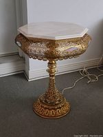 Full view of ornate pedestal table showing marble top and brass base with detailed filigree design and wiring visible on floor.