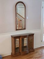Wall mirror mounted above small console display table, wood finishes and glass details visible