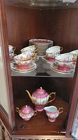 Shelf view showing 12 cups and saucers paired, luncheon plates stacked above, and lower shelf with teapot, sugar bowl and creamer