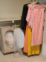 Boxed white wedding dress, hanging veil and beaded purse on floor near clothing rack.