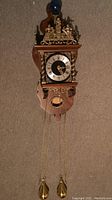 Full front view of clock mounted on backboard showing weights and chain