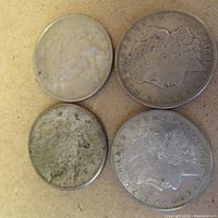 Four American silver dollar coins arranged on a flat surface, showing both sides with visible signs of wear and tarnish.