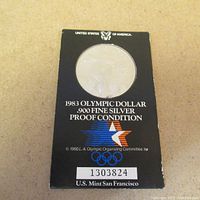 Front of the display case showing the 1983 Olympic Dollar silver coin, the case is black with white text and Olympic logo.