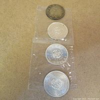 Four Canadian silver dollar coins arranged vertically. Three coins are in transparent protective sleeves and appear shiny. One coin at top is heavily tarnished with darkened surface.