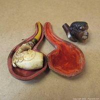 Two carved pipe bowls and one pipe-shaped case with red lining.