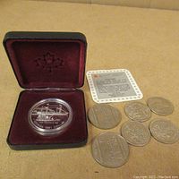 Photo of 1991 Frontenac silver dollar in open red velvet-lined display case alongside six vintage Canadian half dollar coins and a coin information card.
