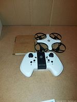 White quadcopter drone and white controller with user manual on cardboard surface