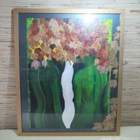 Full view of framed mixed media artwork with white central figure and reddish leaves at top and side.
