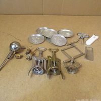 Lot of thirteen items including three wing corkscrews, six round embossed metal coasters with duck design, funnel with cork stopper, bottle opener, bar tap handle, cheese slicer