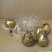 Five faux golden pears and a large clear cut crystal bowl, one pear on small pedestal, against cardboard background.