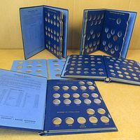 Wide view of multiple blue Canadian coin folders showing coin slots with date labels, some coins present from 1920s to 1950s.