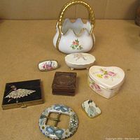 Full lot photo showing assorted small collectibles including porcelain trinket boxes, decorative buckle, compact with ballerina painting, small leather case, and decorative porcelain piece.