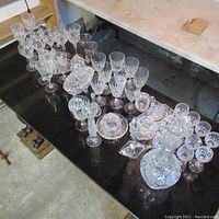 Overview of assorted crystal glassware including stemmed glasses, small bowls, serving dishes on a black surface.