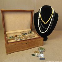 Overview of vintage leather jewelry box open with assorted rings, brooches, small trinket items on the side and four beaded necklaces on display.