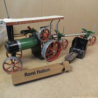 Front and side view of Mamod steam tractor, wooden Royal Hudson train whistle, black metal box, and green metal axle with wheels.