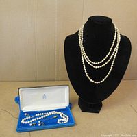 Full view of the lot showing the double-strand pearl necklace on a black display stand and the single-strand necklace, earrings, and brooch inside a blue velvet box.
