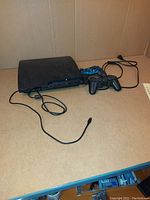 Photo of Sony PlayStation 3 console with two controllers on a wooden surface.