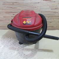 Front view of used red and black Shop-Vac wet/dry vacuum cleaner with flexible black hose attached.