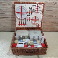 Full view of open wicker picnic case showing plates, cutlery, thermos flasks, salt and pepper shakers inside