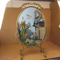 Full view of the oval mirror with the metal frame and painted design on glass.