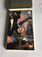 Cover of the 1978 All About Welding book showing a welder in action, holding a welding torch and protective mask with sparks flying.