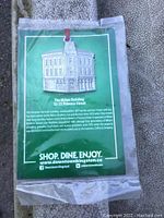 Front view of the pewter ornament packaged on an informational card showing The Milan Building and promotional text for downtown Kingston.