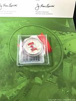 Photo showing the silver coin housed in sealed protective packaging resting on top of a green background with signatures of Royal Canadian Mint officials.