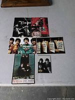 Photo showing all 6 Beatles postcards laid out on a table, showing different colorful and black-and-white images including the Sgt. Pepper uniform, London Palladium poster, multilingual love card, and group photos.