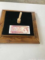 Front view of the 1974 Canadian two dollar note showing Queen Elizabeth II and denomination details displayed on a raised wooden stand with black felt.