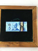 Front side of a Canadian 5 dollar banknote with portrait of Sir Wilfrid Laurier, displayed in a wooden frame with dark fabric background.