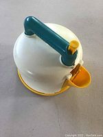 Top and side view photo of the vintage Fisher-Price whistling toy teapot showing the blue-green handle with yellow whistle button, white body, and yellow spout and base.