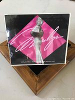 Front view of the Marilyn Monroe stamp souvenir sheet showing the statue image, pink background, and signature with original cellophane intact.