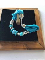 Close-up front view of the modern necklace featuring blue fabric strands and turquoise and metallic beads on a black velvet display.