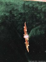 Front view of the gold-tone brooch showing teardrop opal and wing-like design sides on green velvet background.