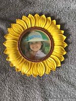 Bright yellow sunflower-shaped photo frame with circular photo opening showing a child's picture. Frame size approx. 8x8 inches with 4-inch diameter circular center.