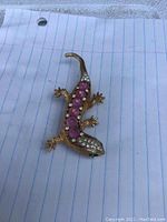 Clear photo of vintage lizard brooch showing pink stones on back, clear rhinestones on head and tail, and green eyes.