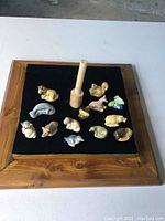 Top view of 13 Wade ceramic animal figurines arranged on black velvet inside a wooden tray with central wooden stand.