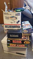 Stack of board games including Pictionary, Risk, Monopoly, and boxes containing other items.