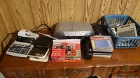 Full lot view including Canon adding machine, Sony radio cassette, assorted calculators, Panasonic cordless phone, calculator manuals and a plastic basket with more calculators.