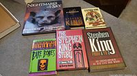 Six Stephen King books laid out on a table, showing covers and titles. The books vary in size and cover design, all appear to be first printings as per seller.