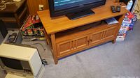 Front view of medium brown wooden TV stand with flat top, two doors, and a television on top.