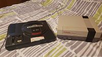 Nintendo Entertainment System and Sega Genesis consoles side by side on bed.