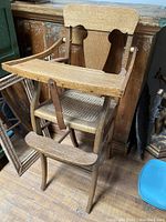 Full view of antique child's chair showing wooden construction, tray, carved backrest, and footrest.
