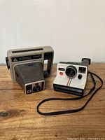 Two vintage instant cameras, Polaroid OneStep and Kodamatic, placed on wooden surface