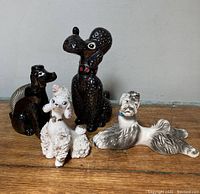 Four vintage poodle figurines on a wooden surface, various colors and styles visible.