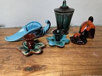 Full view of all five ceramic pieces on wood surface showing a variety of items including candle holders, dog figurine, lidded container and horn dish.