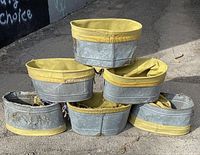 Six vintage galvanized metal apple picking baskets stacked together, showing overall condition and yellow canvas liners folded over rims.
