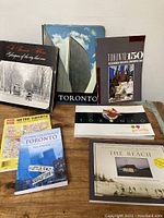 Seven books and booklets with various Toronto themes arranged against a wall, showing cover art and titles to detail contents.