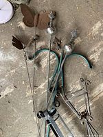 Photo showing multiple metal garden stakes with decorative features including butterfly and orbs with leaves, lying on a floor.
