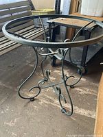 Metal circular patio table base with decorative metal scrollwork legs, showing side view and top support ring.